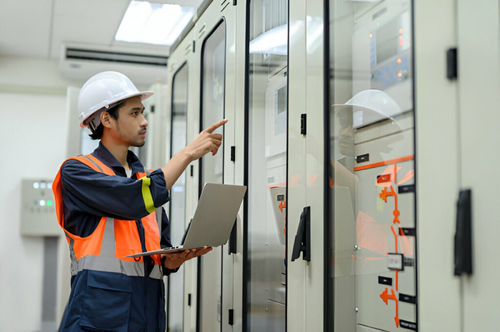 Network engineer with CompTIA Network+ certification checking on check status from control panel switch board in control room of high voltage electric transformer station.